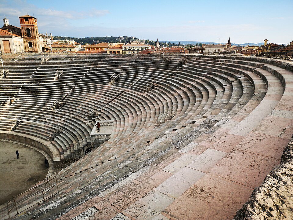 The worn limestone steps of the cavea curving round the arena floor