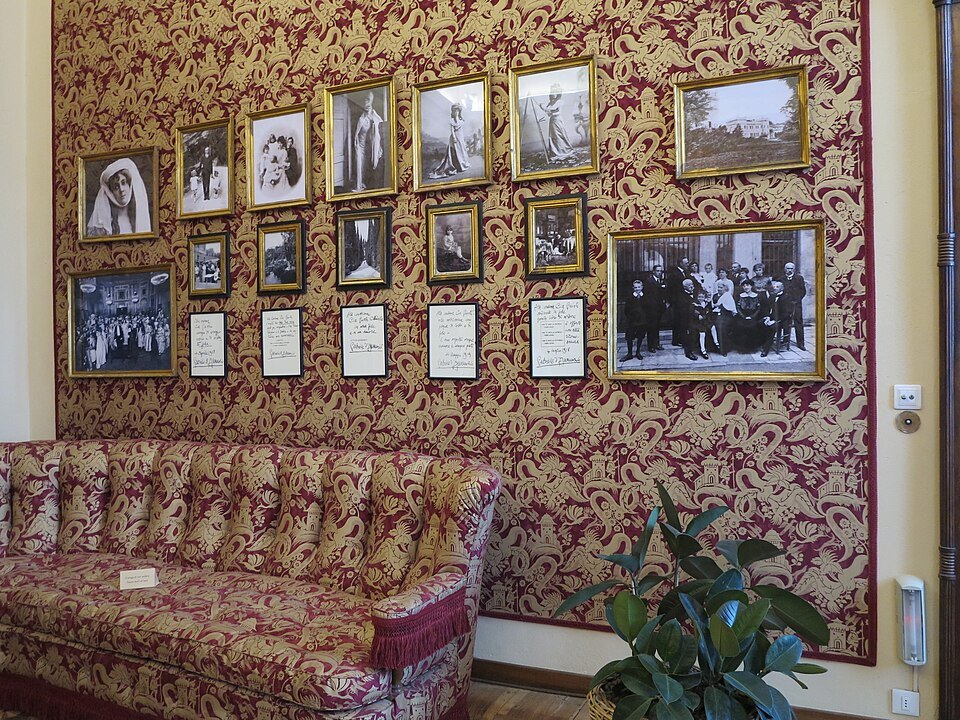 A palace room hung with red damask, portraits on the walls