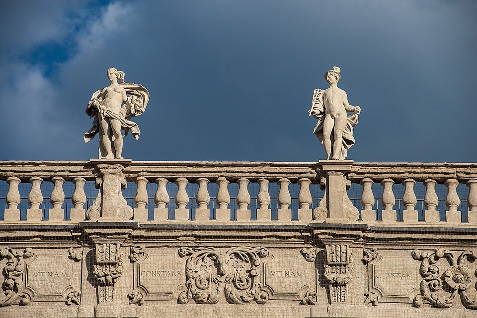 Statues on Palazzo Maffei's balustrade against a dark sky