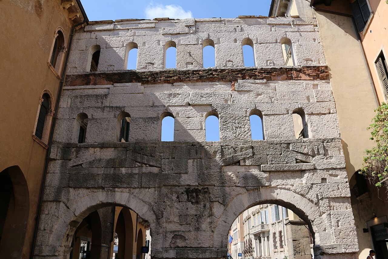 The weathered upper storey of Porta Borsari against the sky